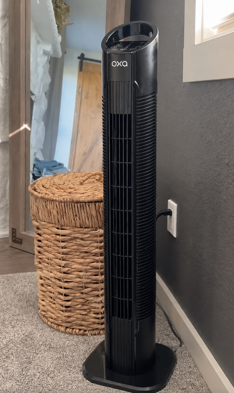 Oxa Tower Fan standing in a corner beside a woven basket